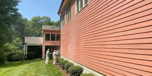 Professional soft washing technicians cleaning a luxury Long Island home exterior with coastal landscaping and blue sky