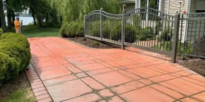 Professional exterior cleaner assessing orange rust stains on concrete driveway in coastal Long Island neighborhood